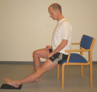 Person sidder på stolekant og strækker benet hen af gulvet på tæppeflise