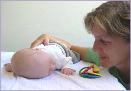 Voksen snakker med et barn som ligger på maven og drejer hovedet mod venstre