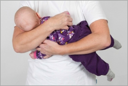 Voksen bære barn sideliggende med maven mod mave og bøjer barnets hoved mød højre med armen