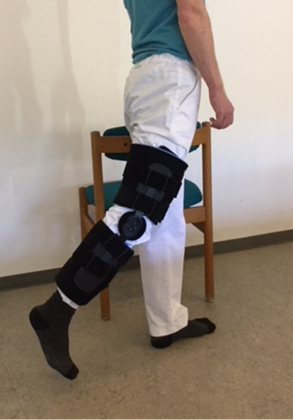 Person med hængselbandage på knæet står ved stol og løfter benet bagud