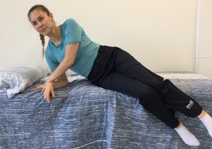 Person er p&aring; vej op i siddende stilling med hj&aelig;lp fra albue og h&aelig;nder. Benene svinges ud over sengekanten.