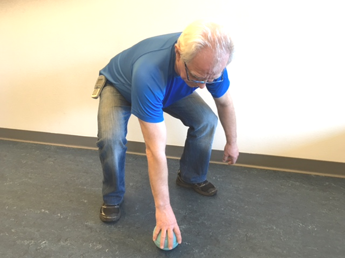 Person står med stor spredning mellem knæene, mens han bukker sig frem for at samle noget op fra gulvet