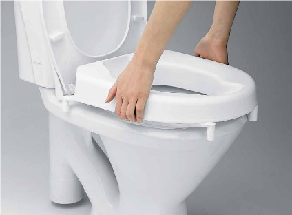 Person er ved at sætte en toiletforhøjer på toilettet, hvor sædet er slået op.
