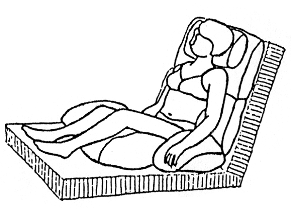 Person sidder i seng let tilbagelænet med pude under knæ og bag nakke