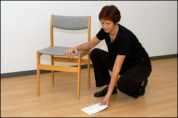 Person støtter sig på en stol, mens hun bøjer ned på knæ for at samle noget op