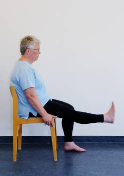 Patienten sidder tilbage på en stol. Det ene ben er bøjet, det andet ben er løftet og strakt.