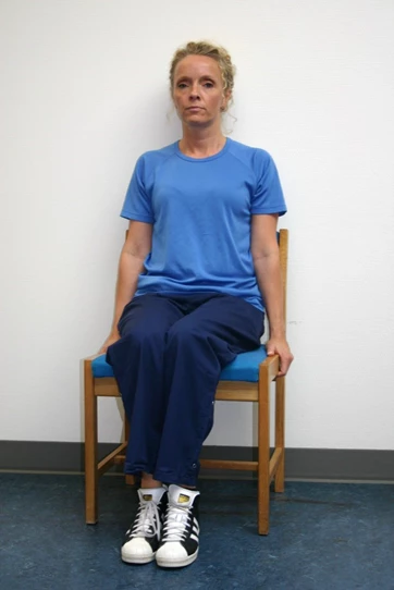 Kvinde sidder på stol og trækker opad med hænderne på sædet