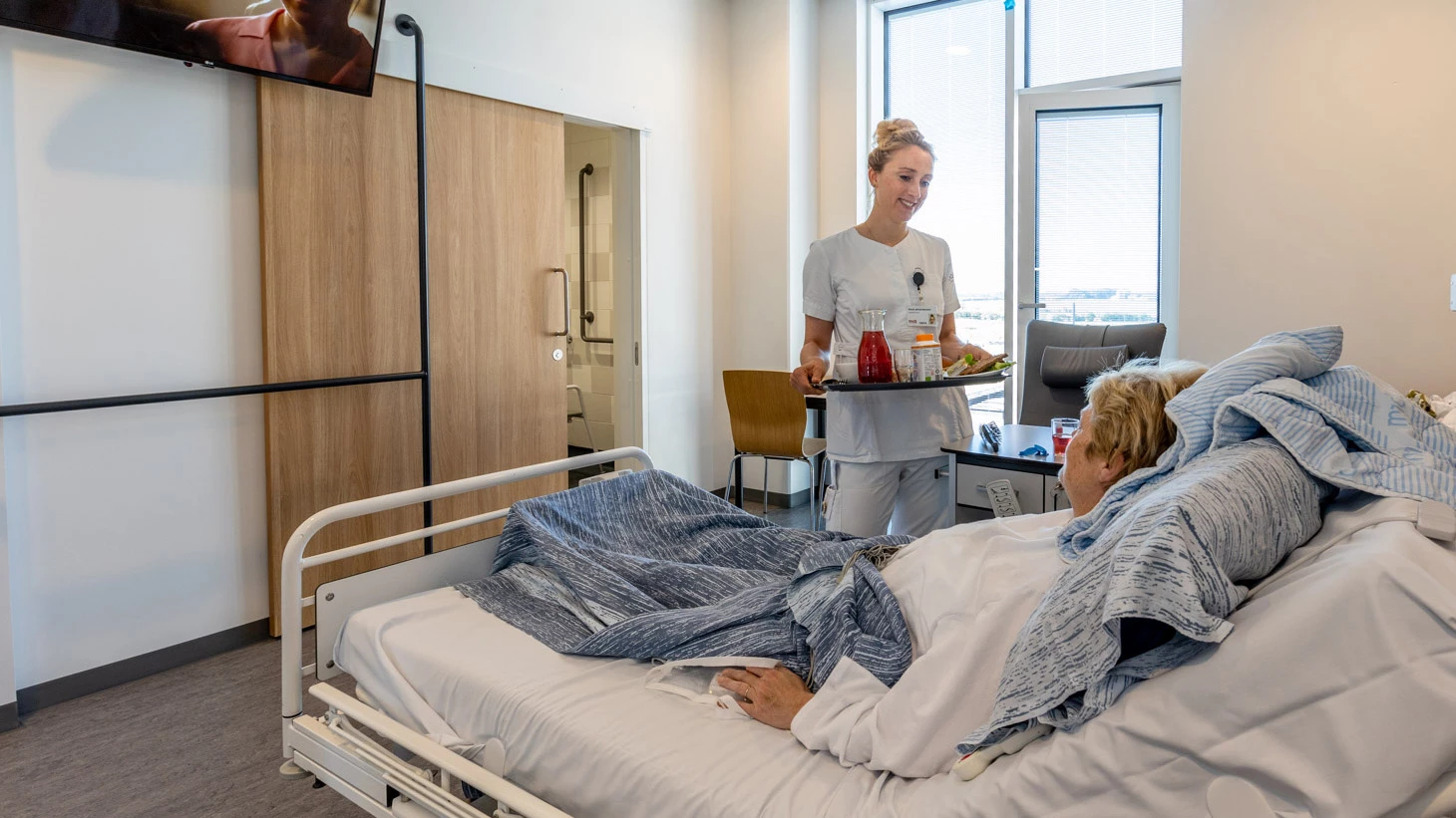 Sygeplejerske med bakke på sengestue