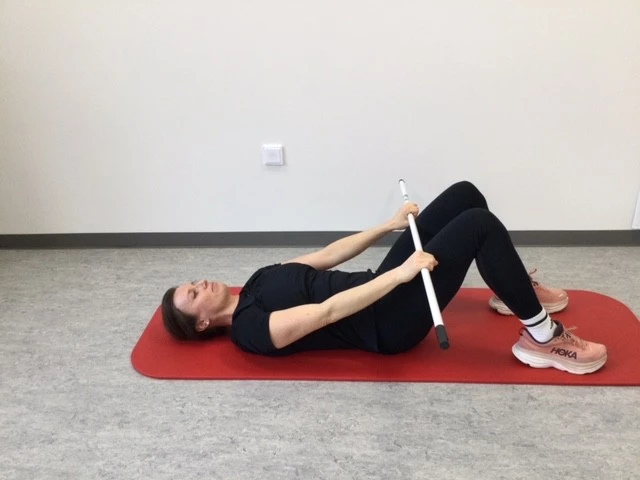 Kvinde ligger på ryggen med pind i strakte hænder ned mod låret