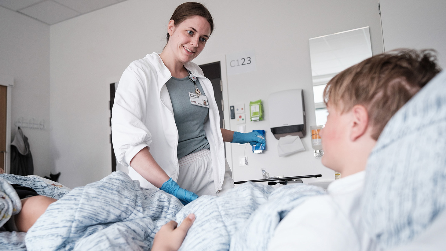 Sygeplejerske snakker med en dreng, der ligger i en hospitalsseng.