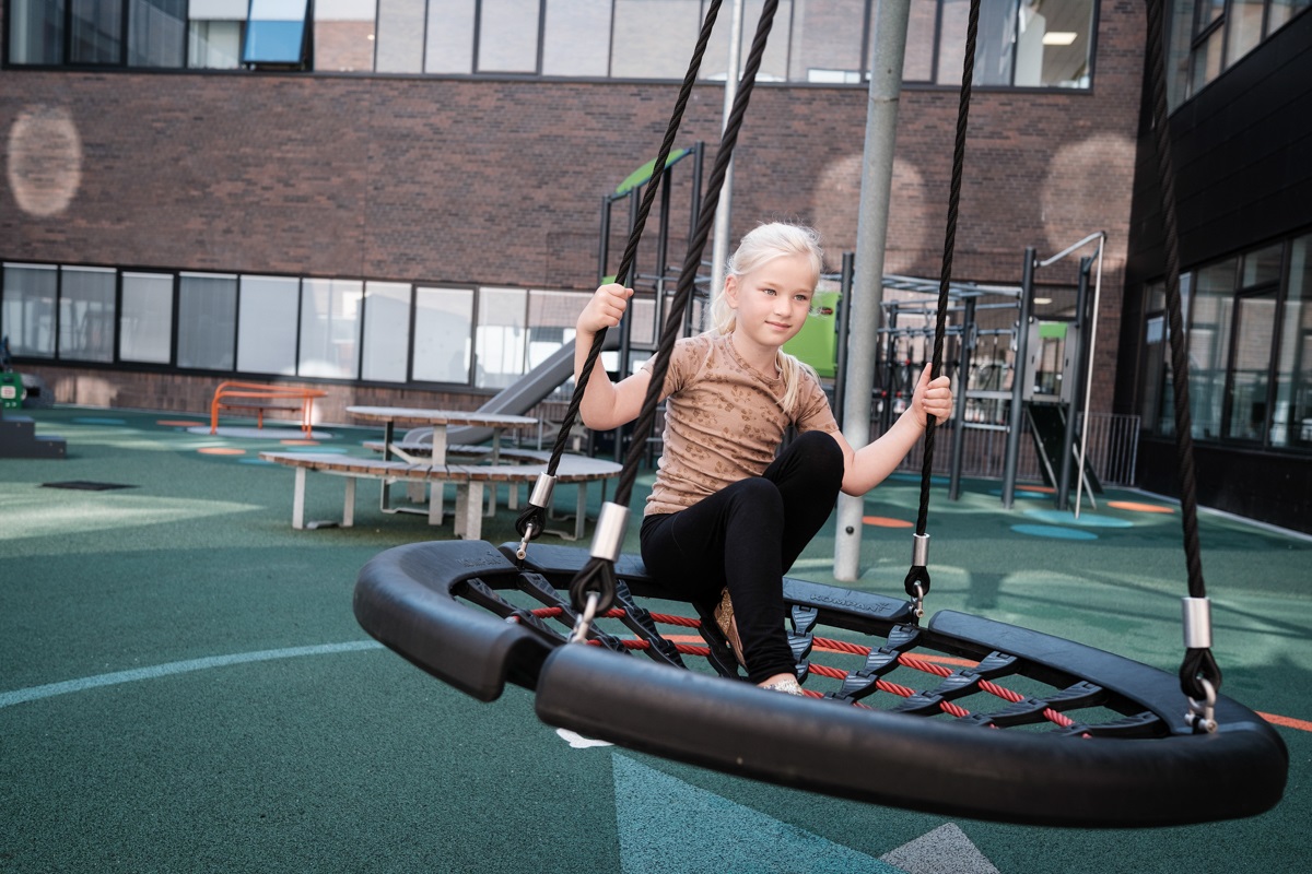 Pige sidder på en sansegynge på Regionshospitalet Gødstrups legeplads.