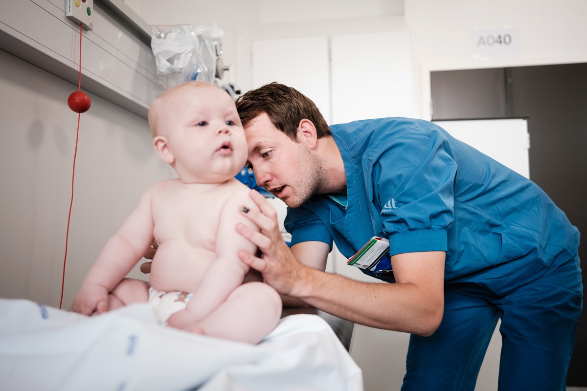 Mandlig læge i blå uniform undersøger en babys ryg.