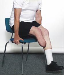 Person med et underben amputeret sidder på en stol, sætter armene i stolesædet og løfter numsen fri af stolen