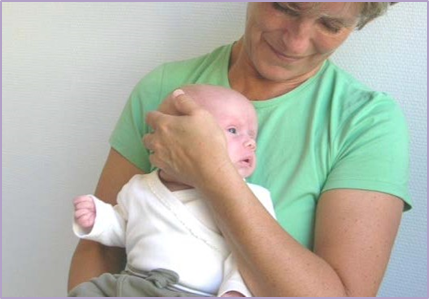 Voksen holder et barn med ryggen op mod den voksnes mave og en hånd drejer barnets hoved til venstre