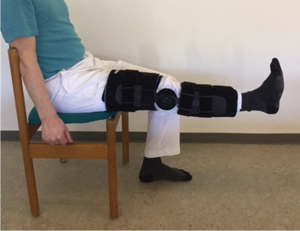 Person med hængselbandage sidder på en stol og strækker benet op