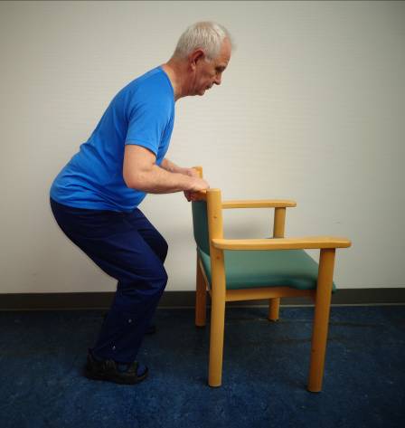 Person holder ved ryglæn på stol og laver knæbøjninger